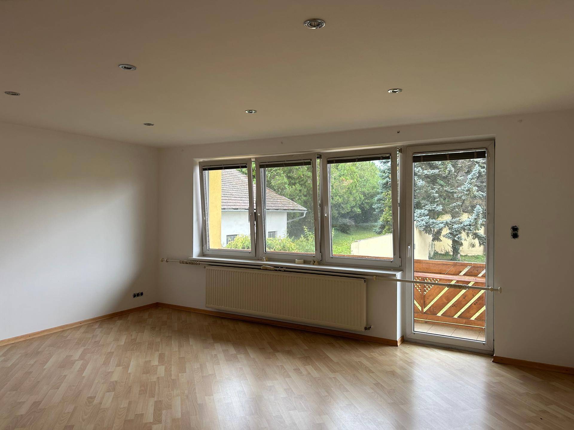 Heller Wohnraum mit Laminatboden, großen Fenstern und direktem Zugang zu einem Balkon.