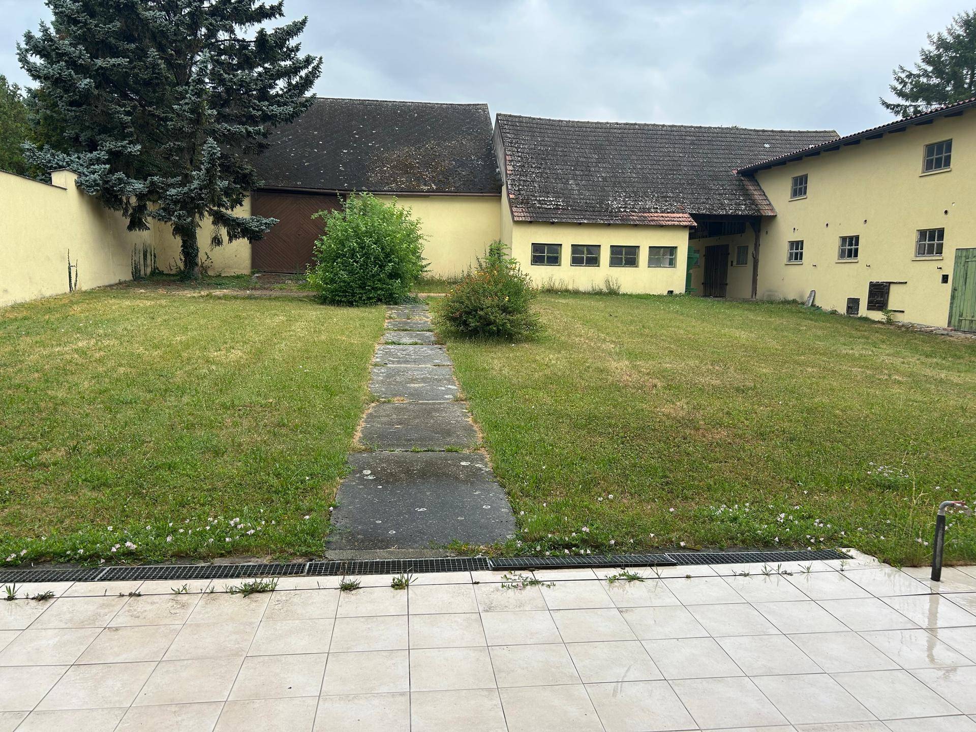 Großer Gartenbereich mit Rasenfläche und einem gepflasterten Weg, umgeben von Bäumen.
