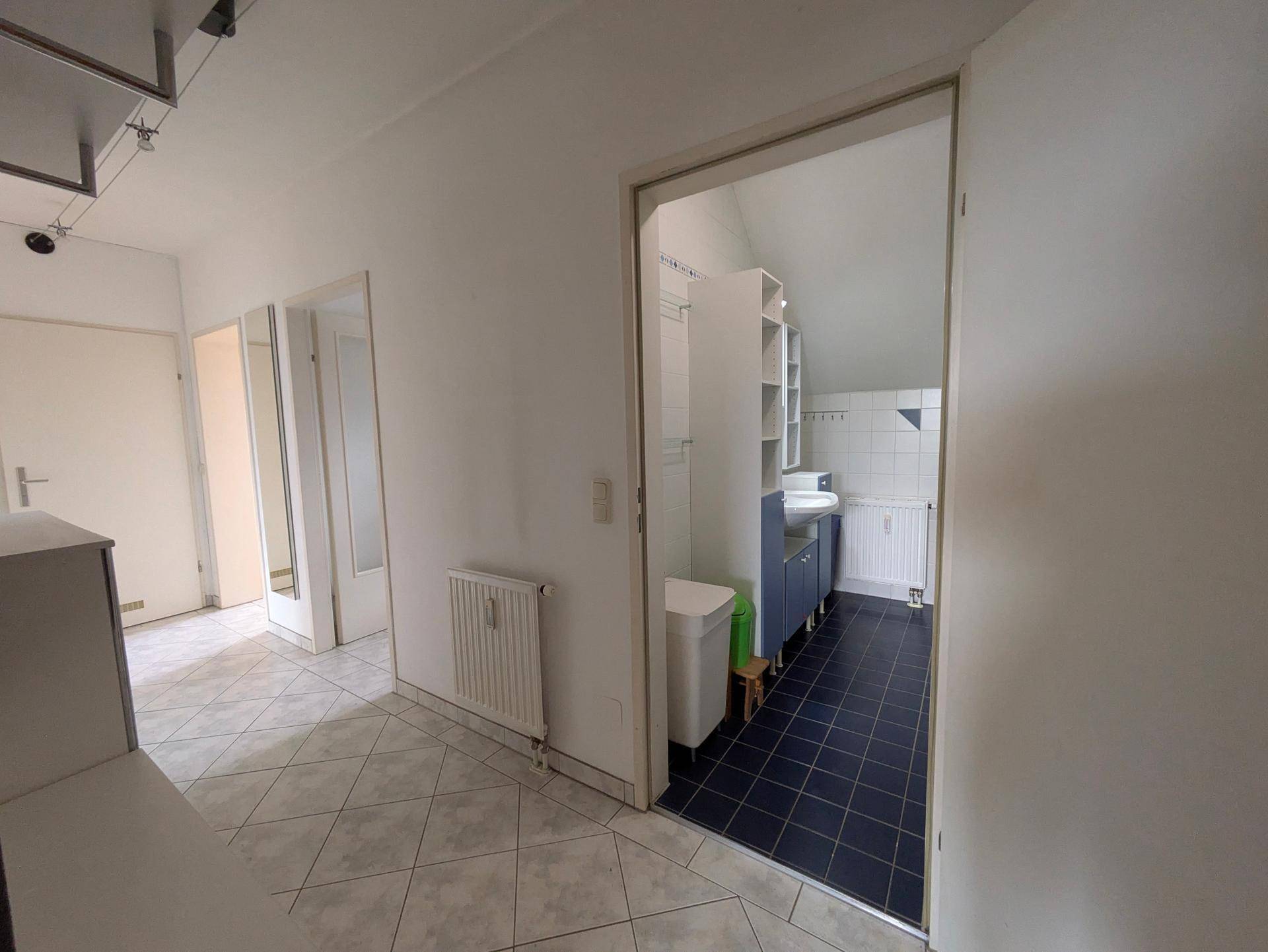 Flur mit Fliesenboden, der zu einem Badezimmer mit blauen Akzenten führt.