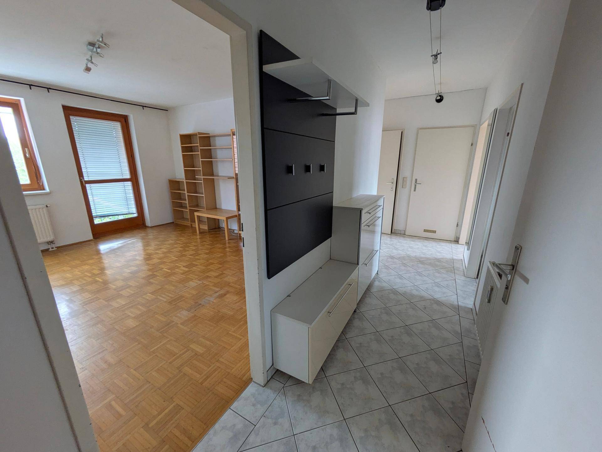 Heller Eingangsbereich mit Fliesenboden und Garderobe, offen zum Wohnzimmer.