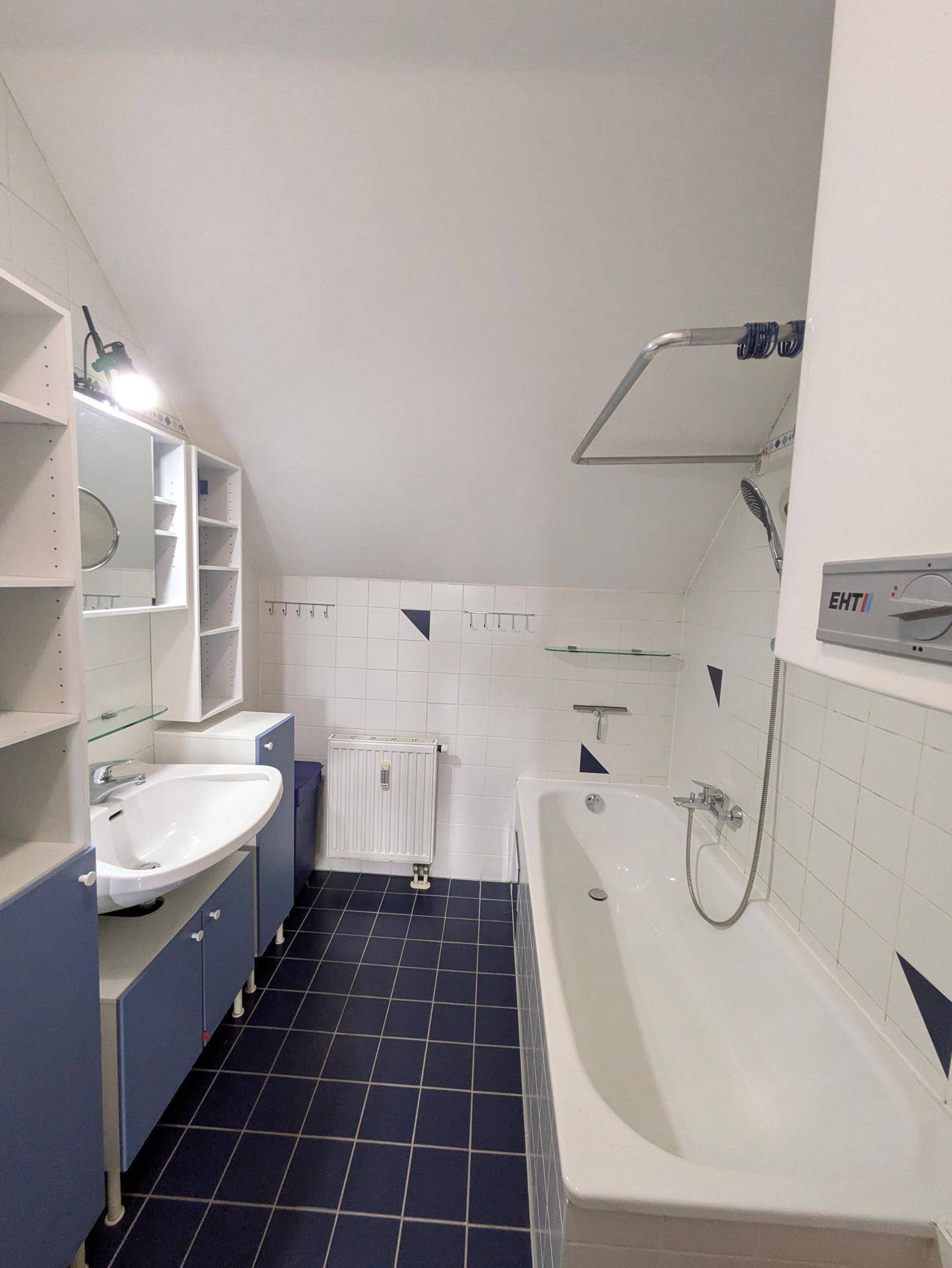 Badezimmer im Dachgeschoss mit Badewanne, Waschbecken und blauen Bodenfliesen.