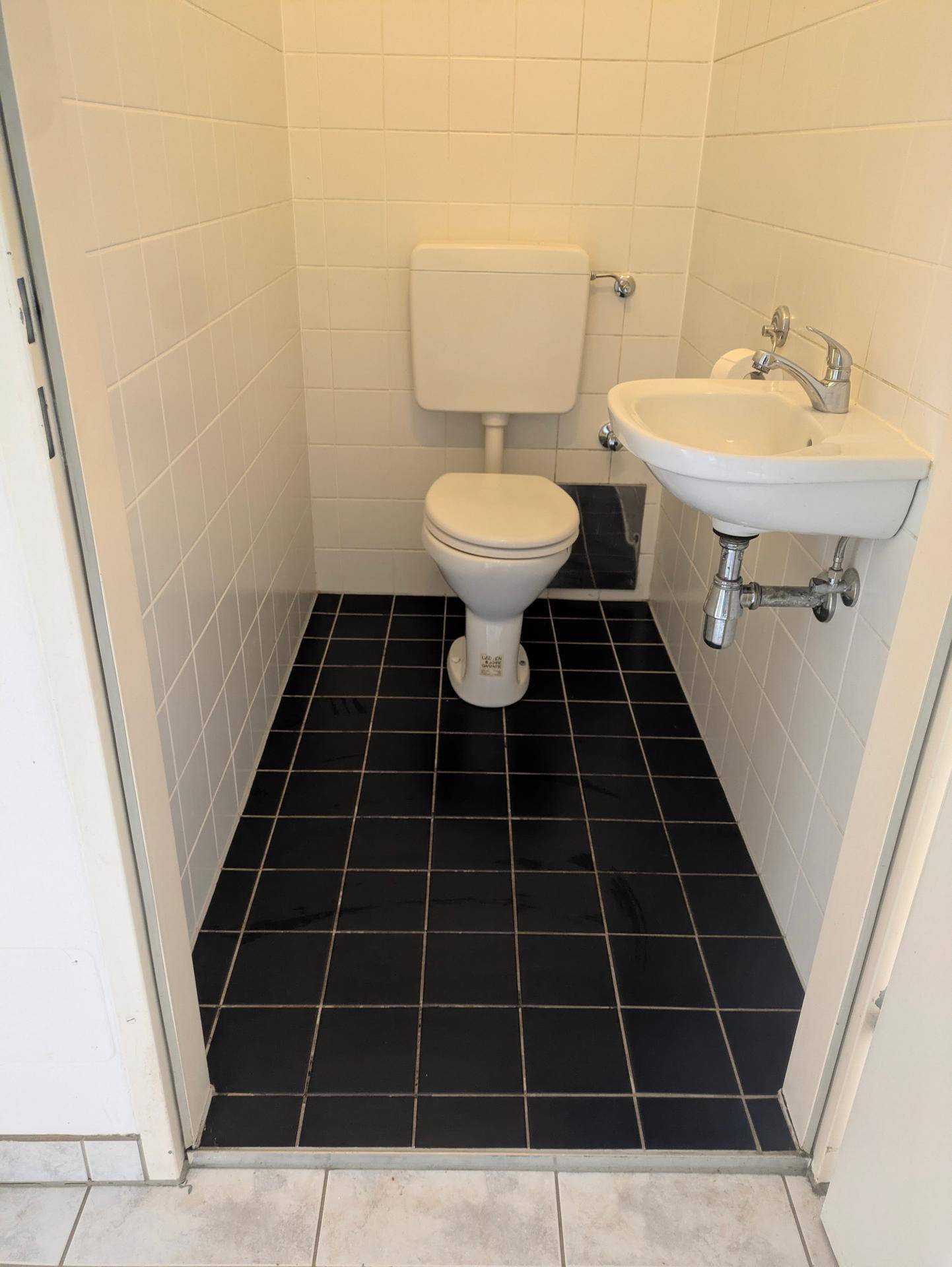 Kleines Gäste-WC mit weißen Wandfliesen und dunklem Fliesenboden.