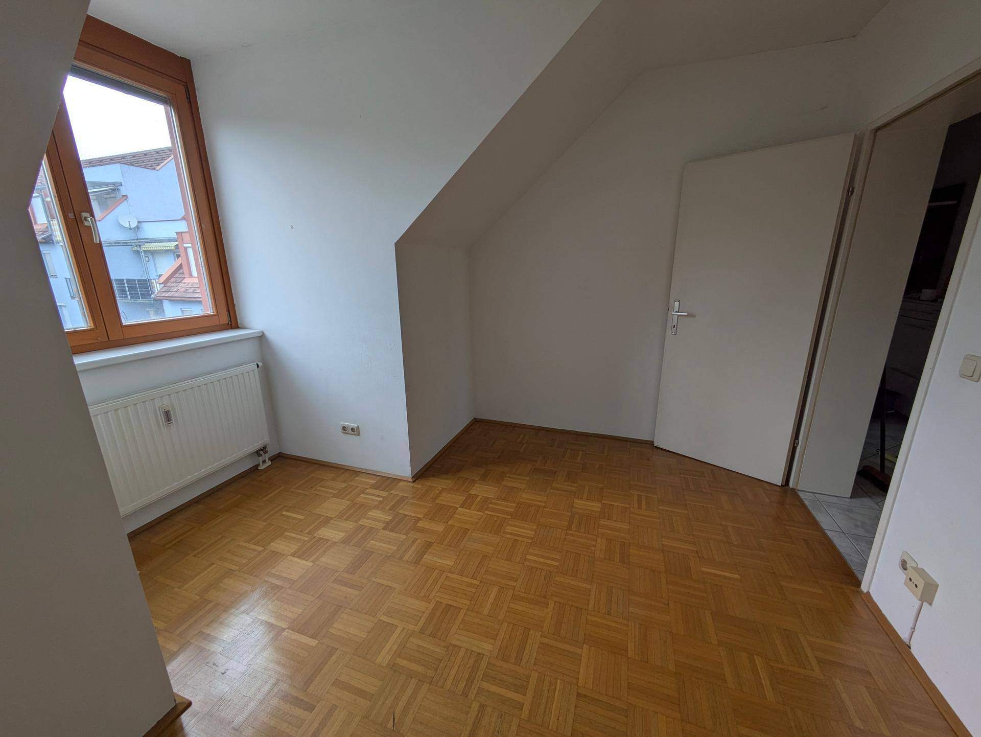 Weiteres Schlafzimmer im Dachgeschoss mit Parkettboden, Dachschräge und hellem Fenster.