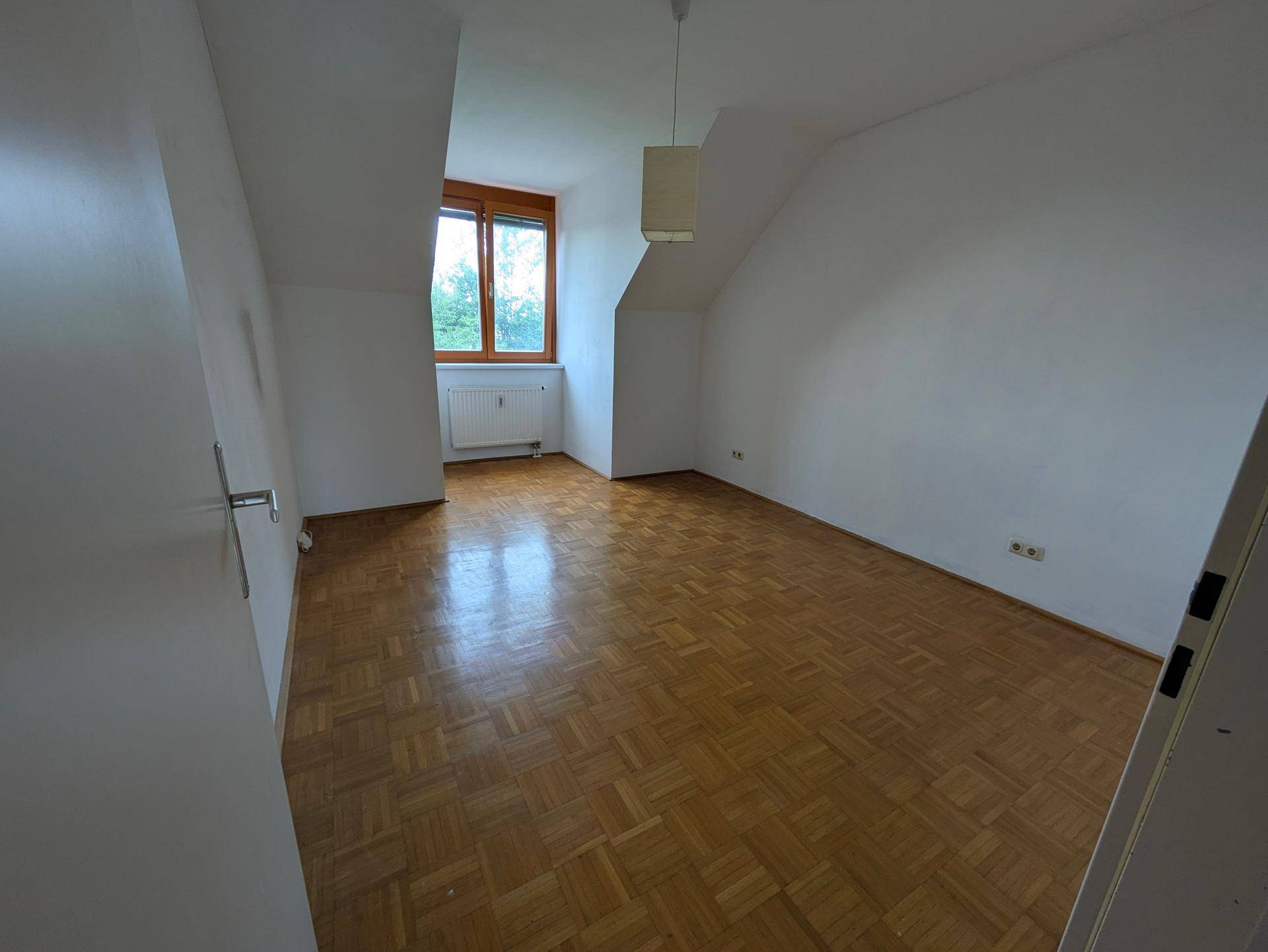 Schlafzimmer im Dachgeschoss mit Parkettboden, Dachschräge und einem Fenster mit Ausblick.