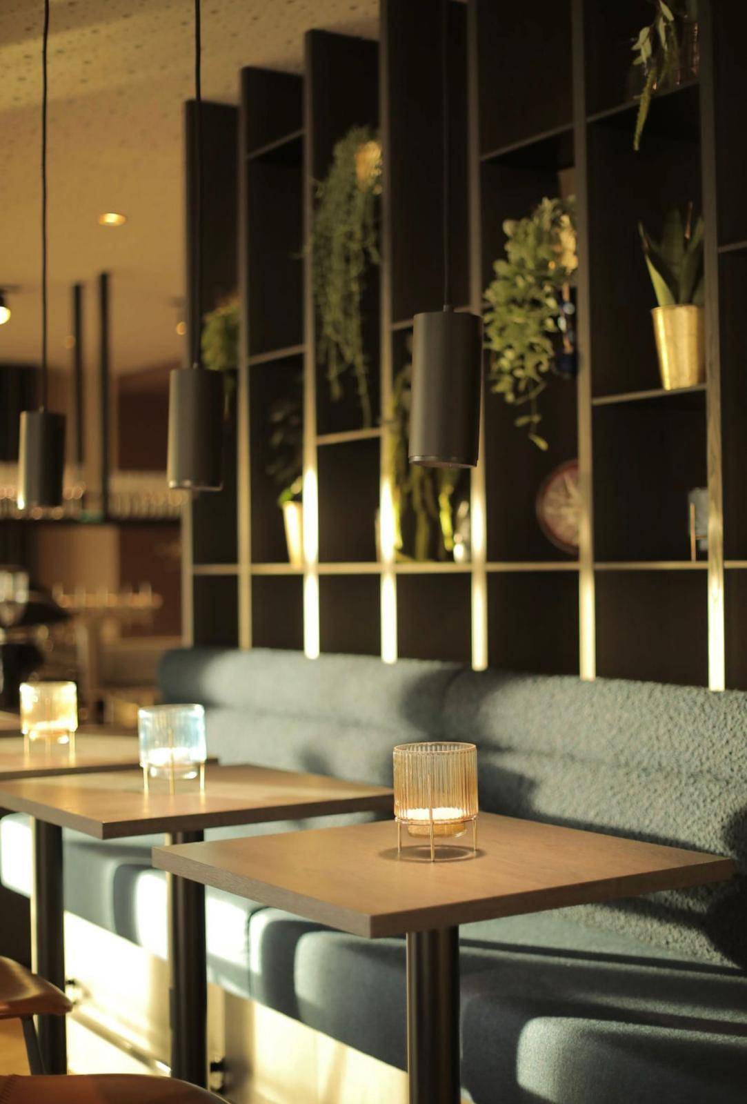 Detailansicht der Sitzbänke und Tische im Restaurantbereich mit dekorativen Kerzen und Pendelleuchten.
