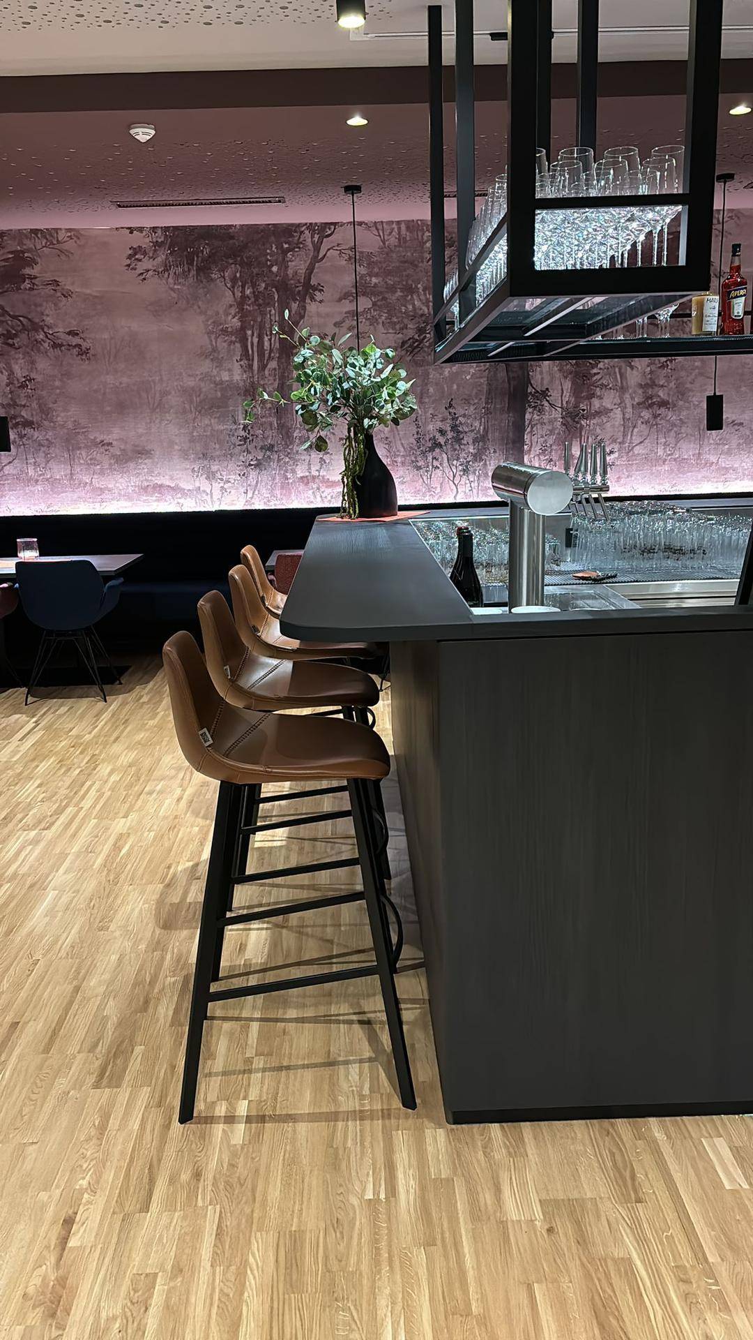 Seitenansicht der Bar mit braunen Barhockern, einer dunklen Theke und einer Flaschenauslage.