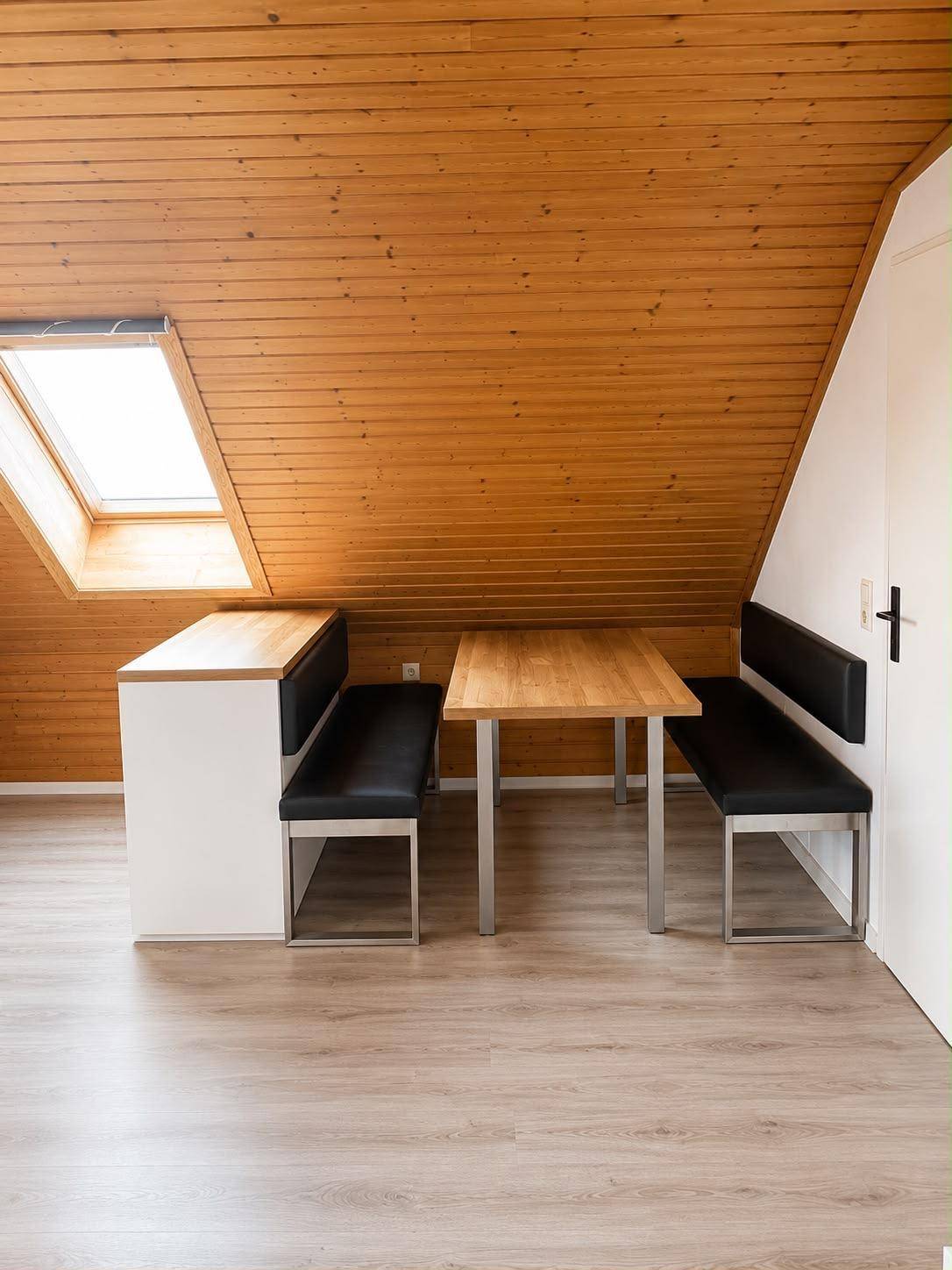 Gemütlicher Essbereich unter einer Holzdecke mit Dachfenster und Holztisch.