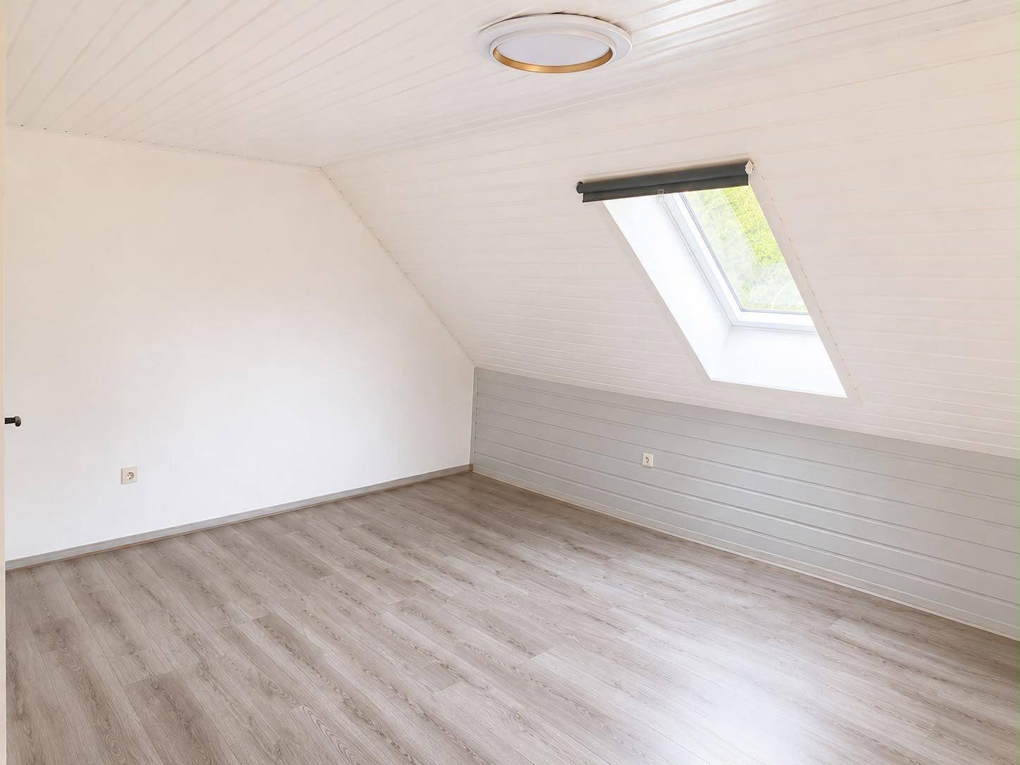 Geräumiges Zimmer mit weißer Holzdecke, Laminatboden und Dachfenster.