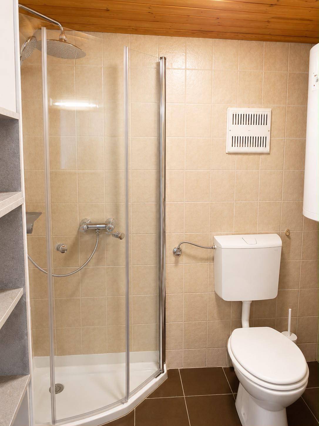 Badezimmer mit beigefarbenen Fliesen, Duschkabine und Toilette.