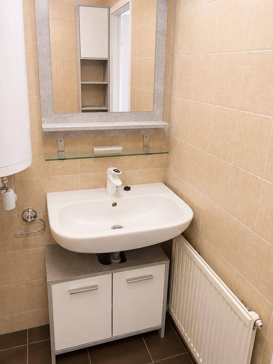 Badezimmer mit Waschbecken, Spiegelschrank und Heizkörper, in beigen Fliesen gehalten.