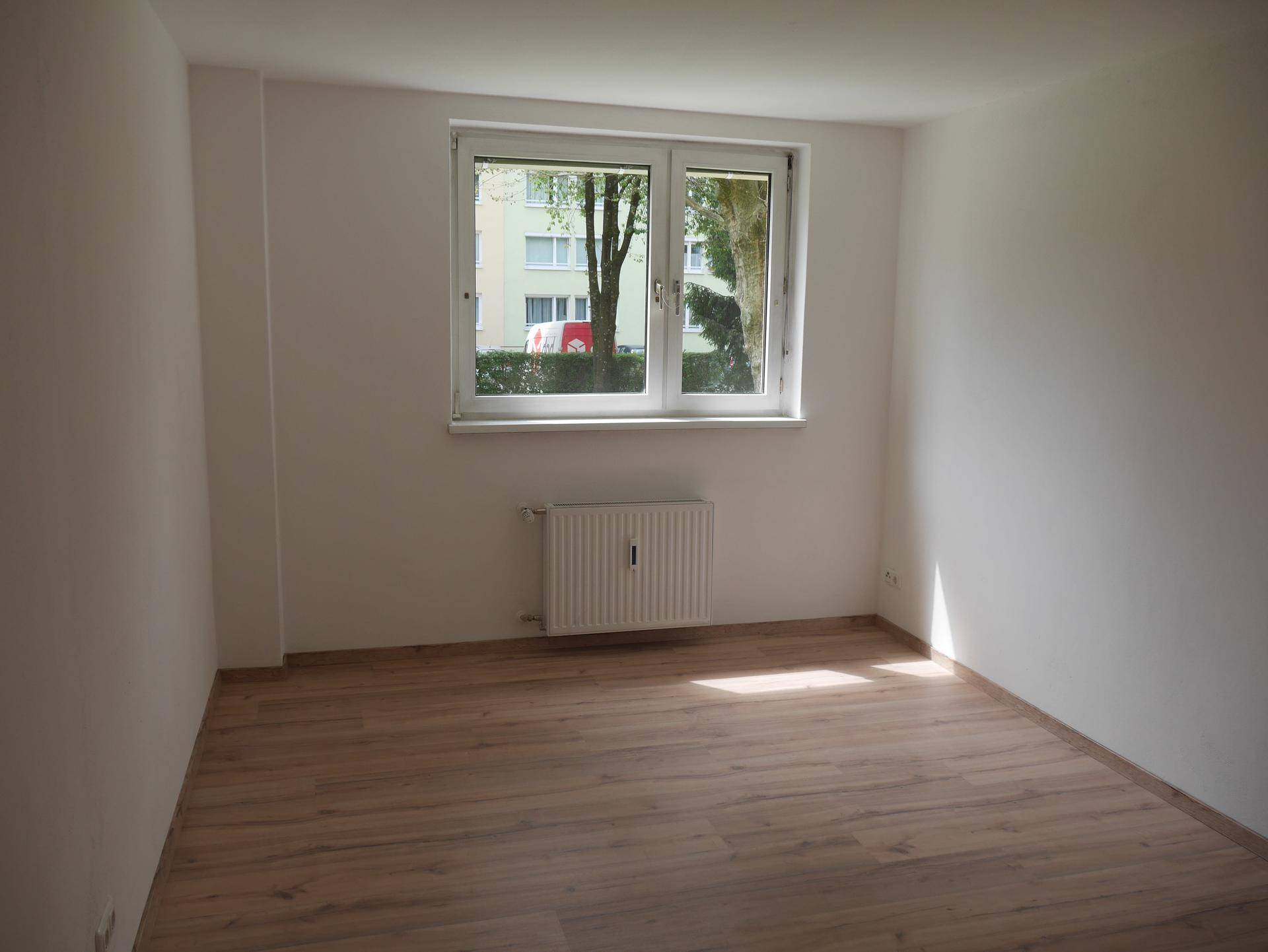 Heller, leerer Raum mit Laminatboden, Fenster und Blick ins Grüne.