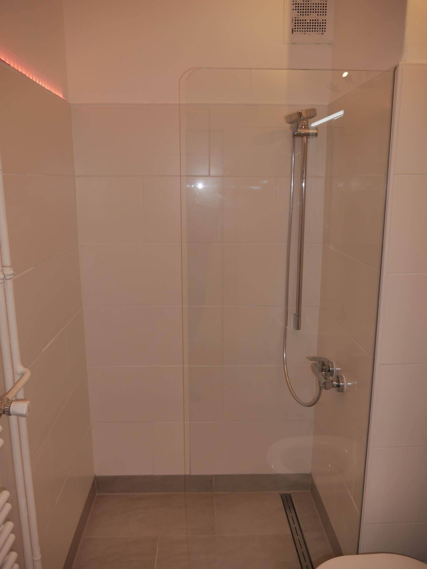 Moderne Duschkabine mit Fliesen, Duscharmatur, Handtuchheizkörper und Deckenlüfter.