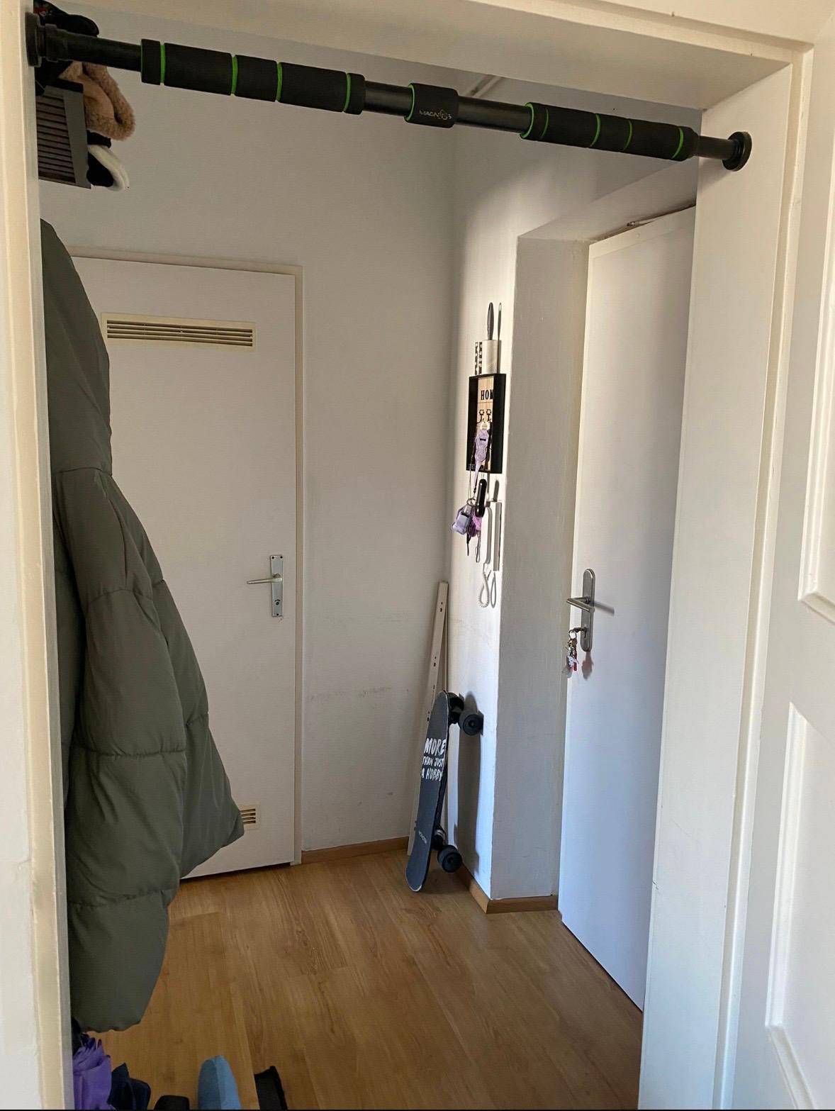 Heller Flur mit Holzboden, Garderobe und einer Klimmzugstange im Türrahmen.