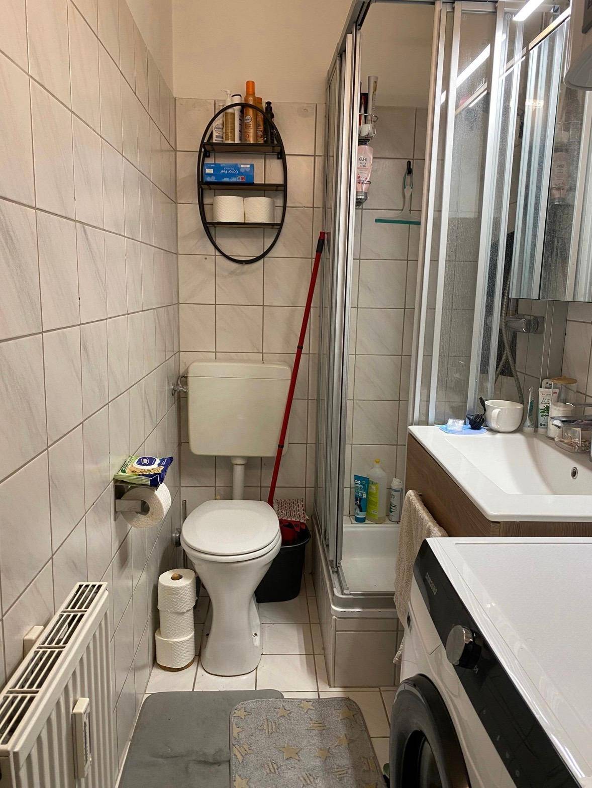 Funktionales Badezimmer mit Duschkabine, Toilette, Waschbecken und Waschmaschine.