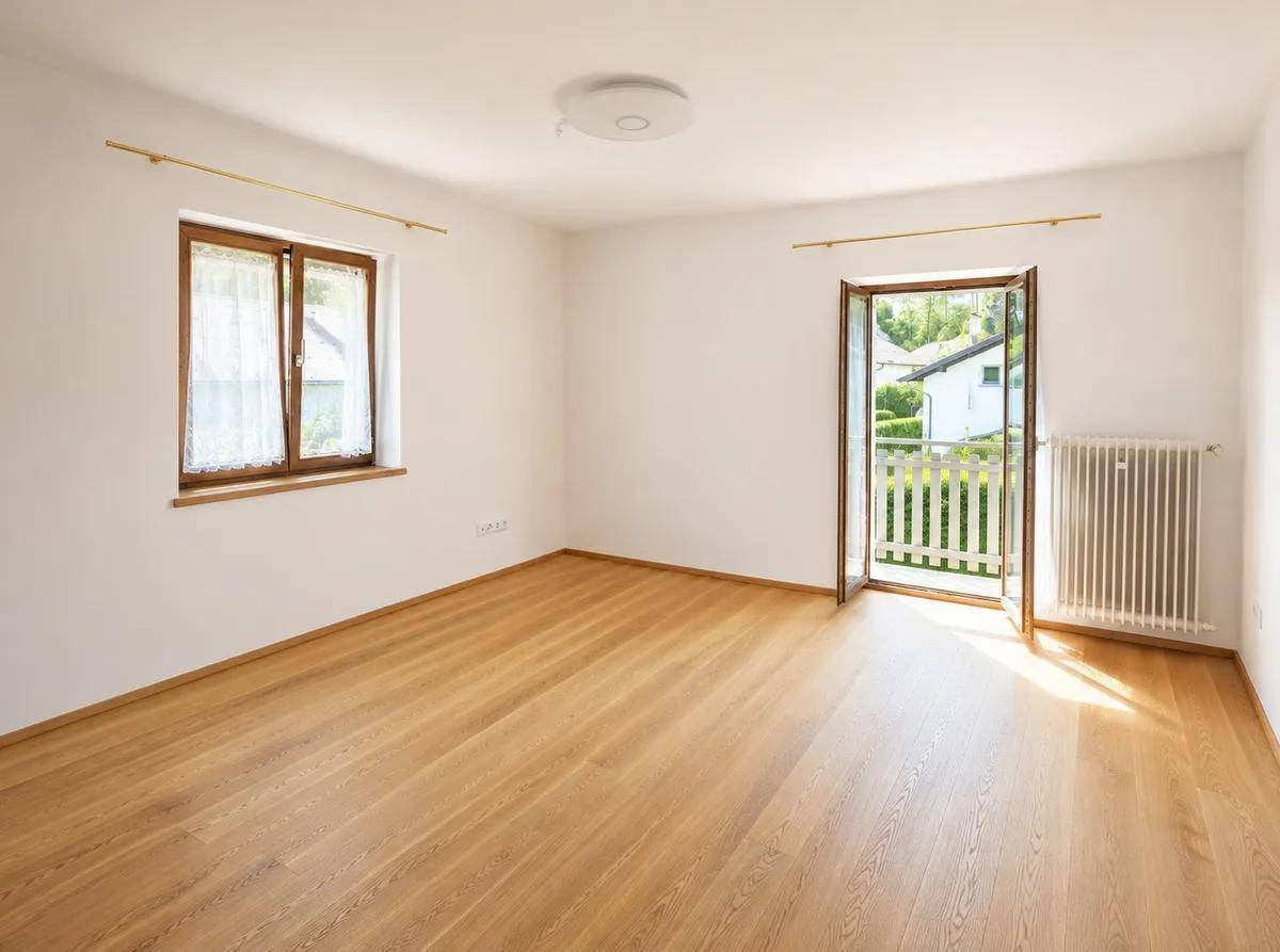 Heller Raum mit Holzboden, Fenster und Zugang zu einem französischen Balkon.