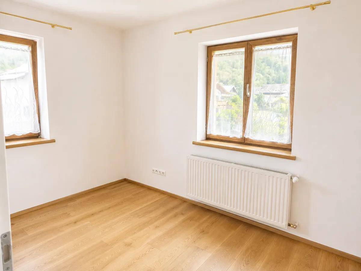 Heller Raum mit Holzboden und zwei Fenstern, ideal als Schlaf- oder Arbeitszimmer.