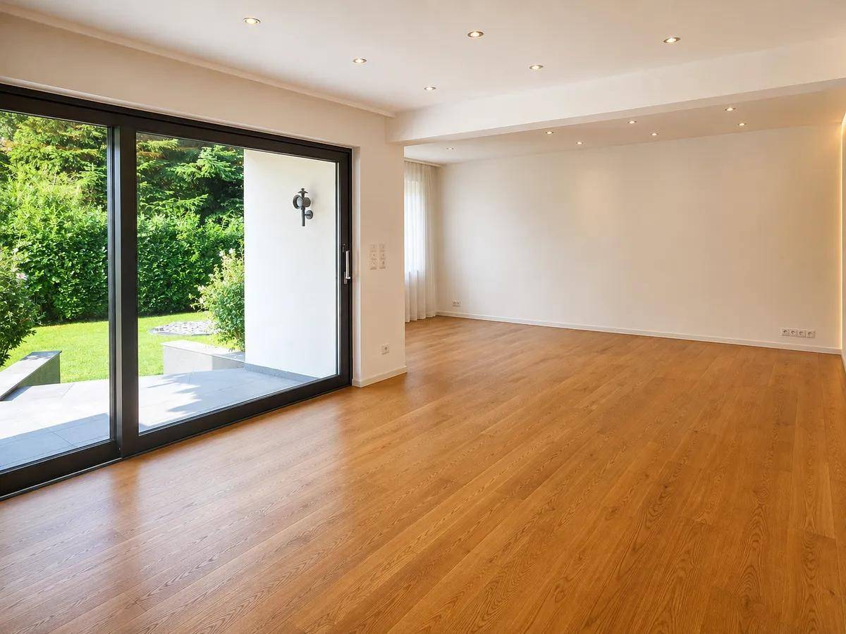 Heller, leerer Wohnbereich mit großen Schiebetüren und Zugang zur Terrasse und Garten.