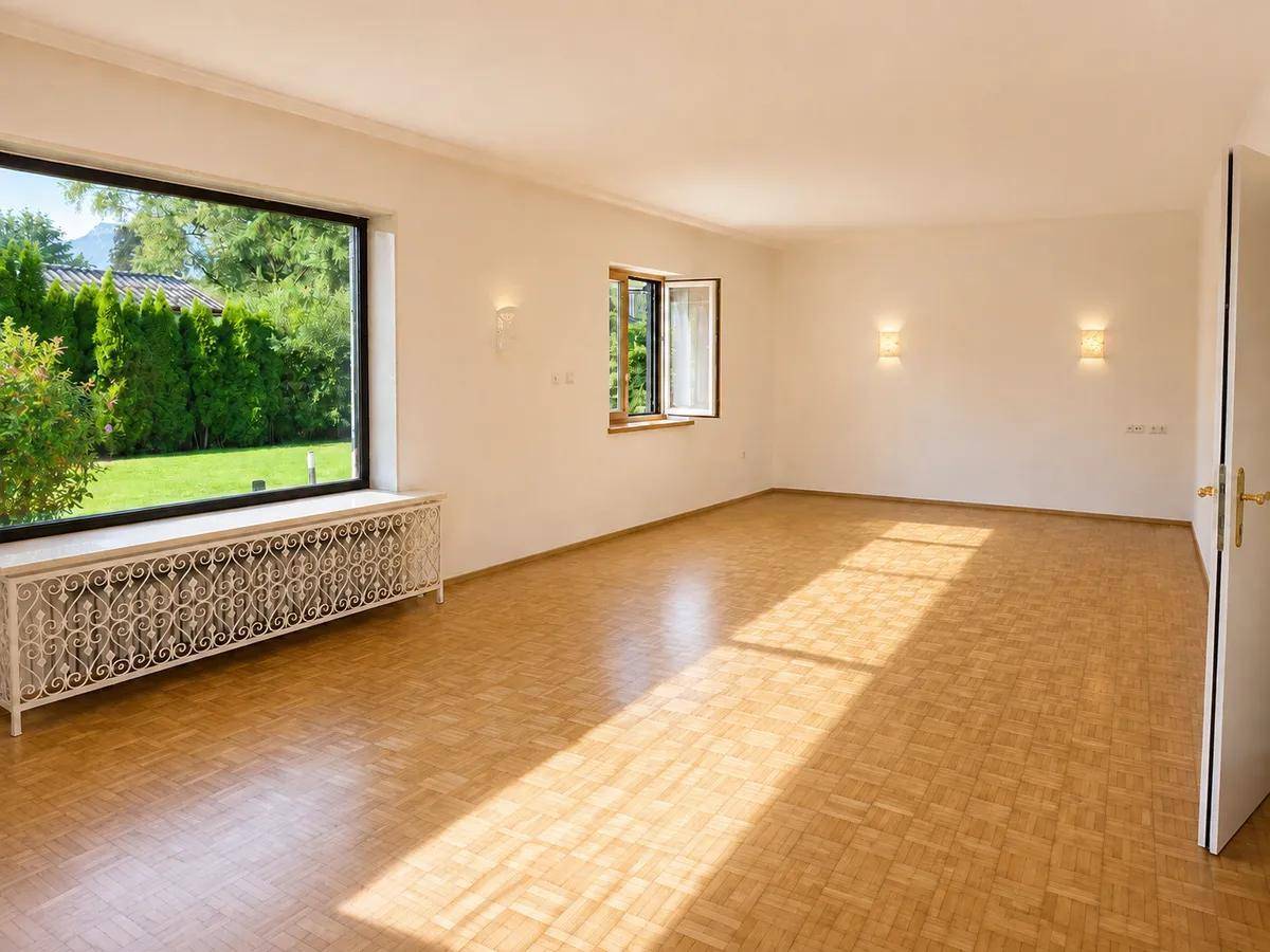 Großer, heller Raum mit Parkettboden, breitem Fenster und Blick in den Garten.