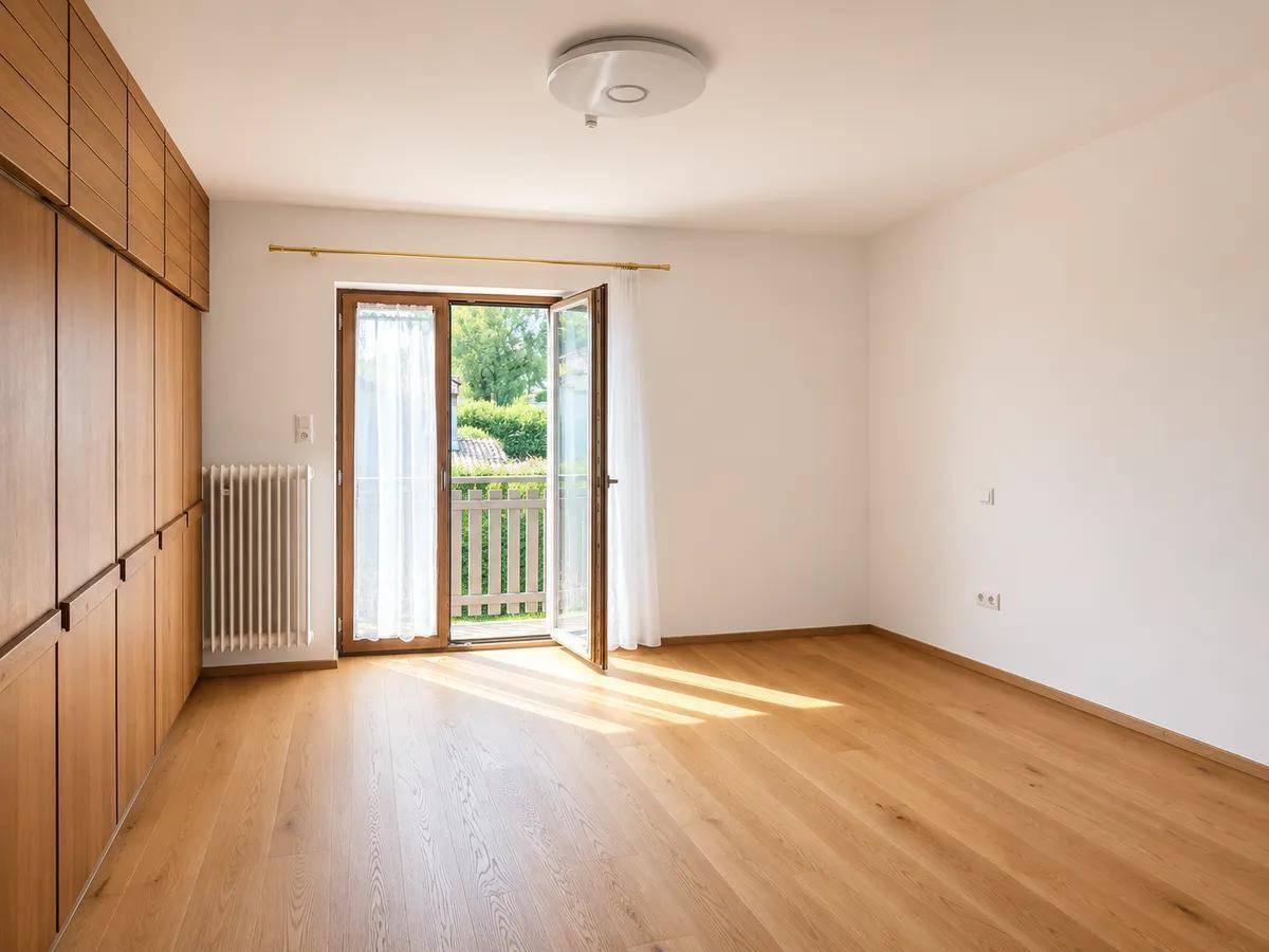 Schlafzimmer mit Holzboden, Einbauschränken und Zugang zu einem französischen Balkon.