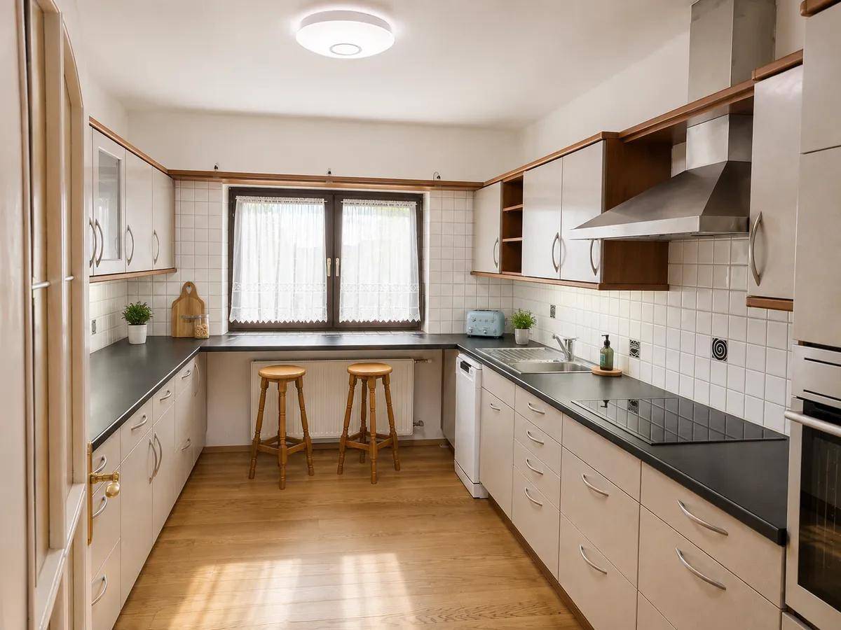 Funktionale Küche mit weißen Schränken, dunklen Arbeitsplatten und Fensterblick.