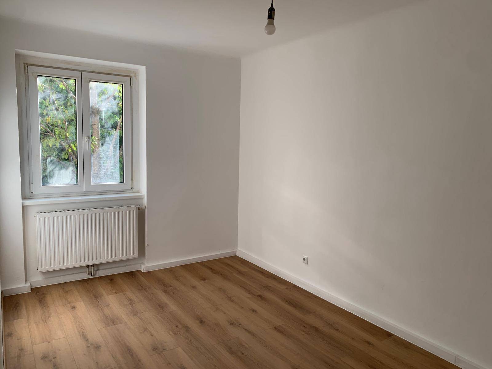 Leeres Zimmer mit Laminatboden, weiß gestrichenen Wänden und einem Fenster.