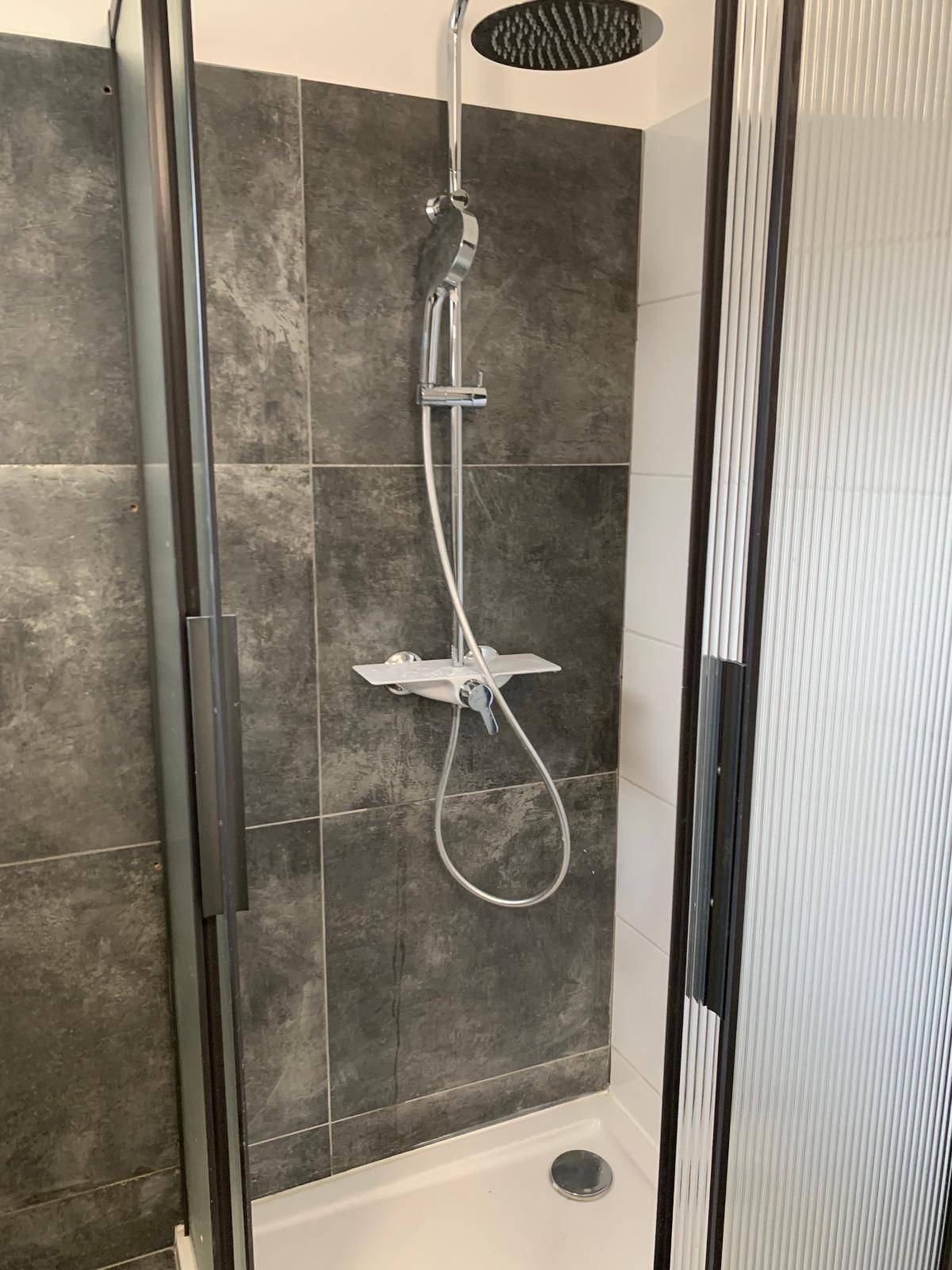Duschbereich mit Regendusche und dunklen Fliesen in einem modernen Badezimmer.