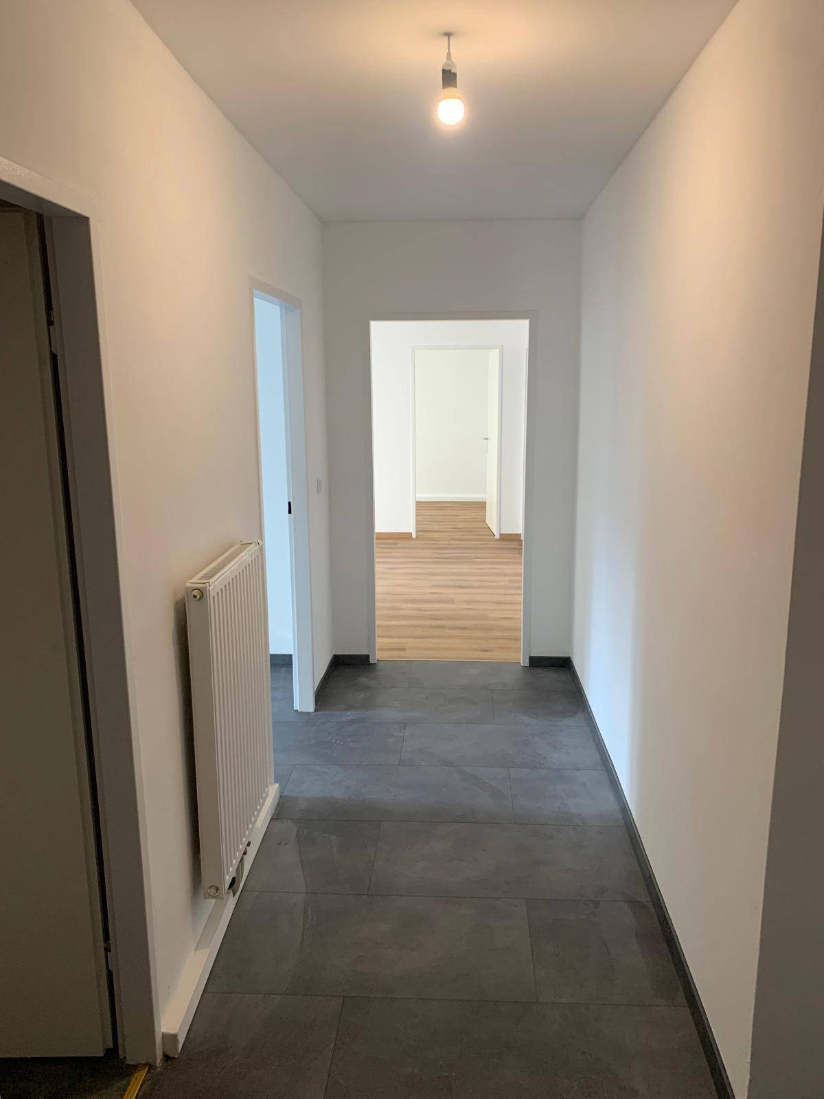 Heller Flur mit dunklen Fliesen und Blick in angrenzende Zimmer mit Laminatboden.