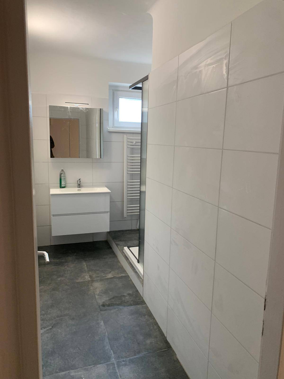 Modernes Badezimmer mit weißen Fliesen, dunklem Boden und Duschkabine.