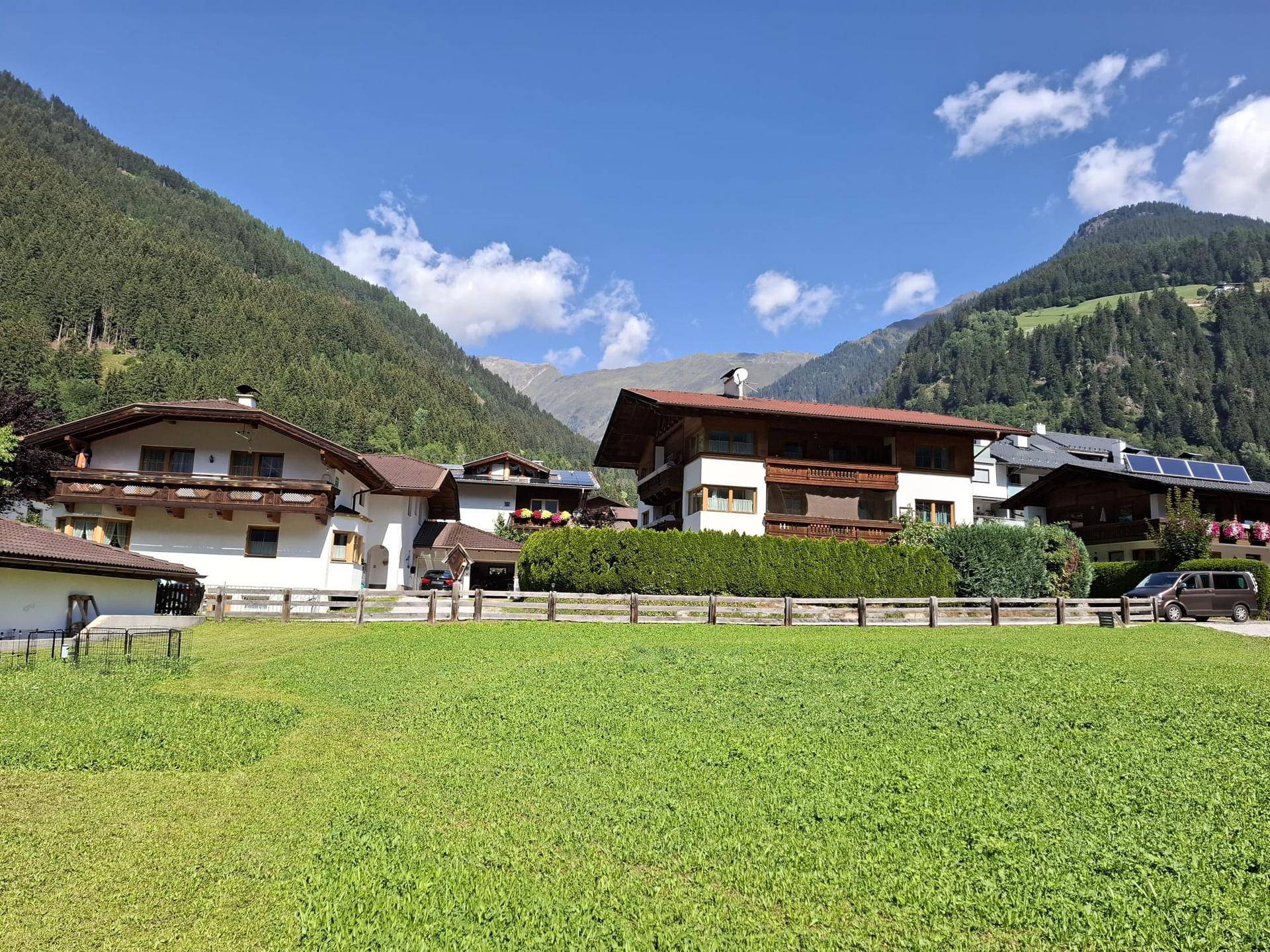 Idyllische Alpenkulisse mit mehreren Häusern und grünen Wiesen unter strahlendem Himmel.