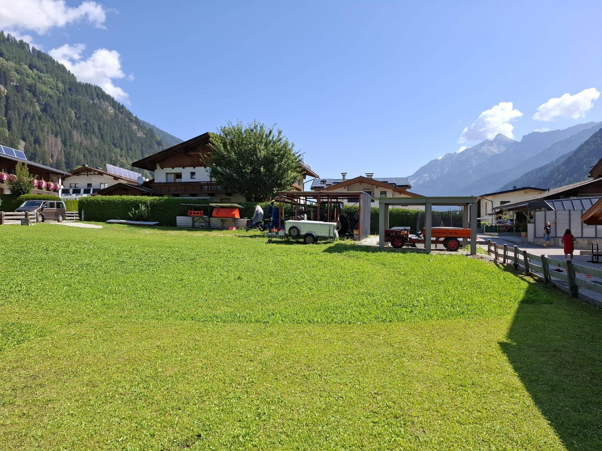 Sonnige Alpenlandschaft mit traditionellen Häusern und weiten Grünflächen.