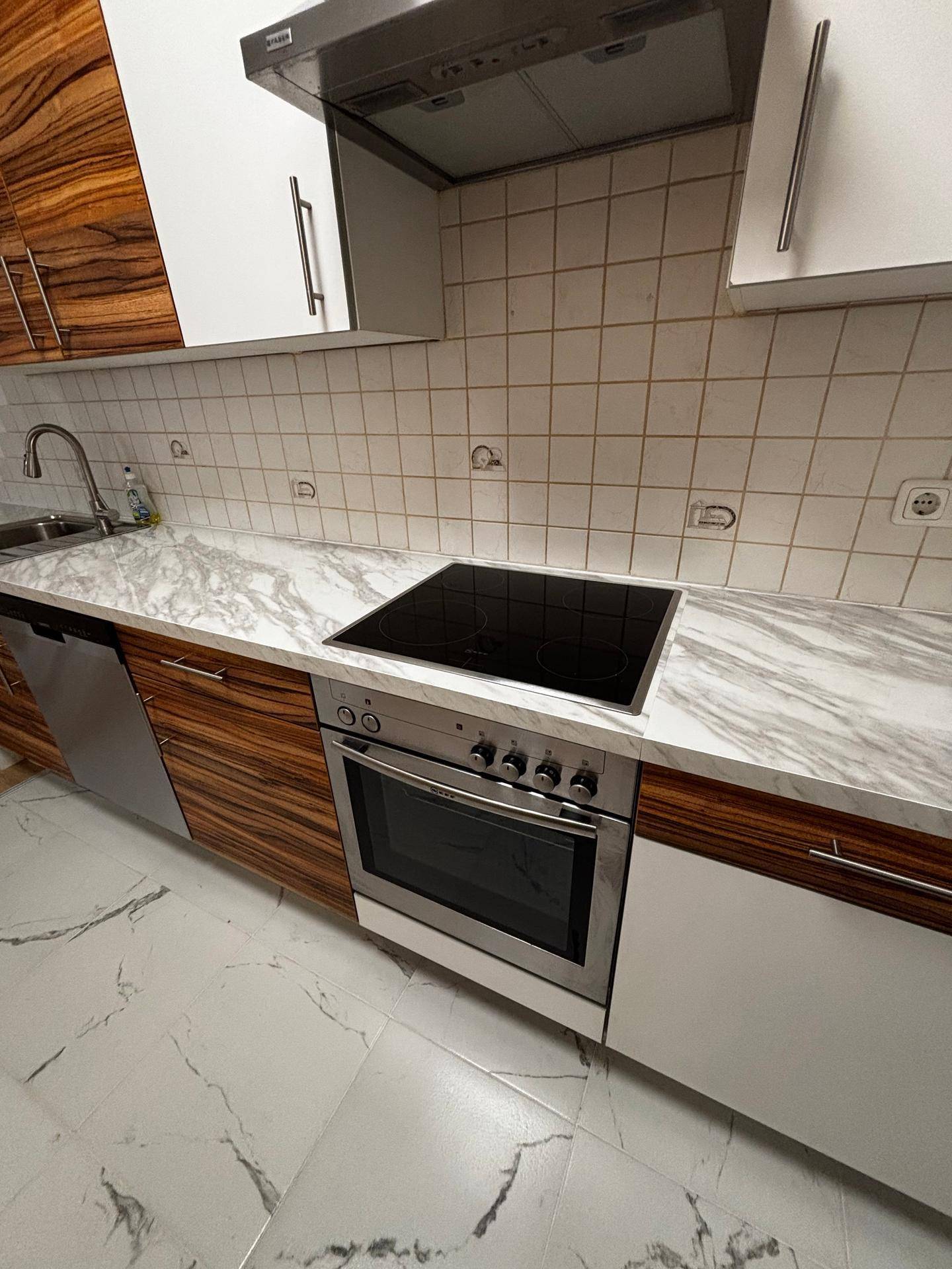 Moderne Küche mit Induktionskochfeld, Backofen und Arbeitsplatte in Marmoroptik, inklusive Geschirrspüler.