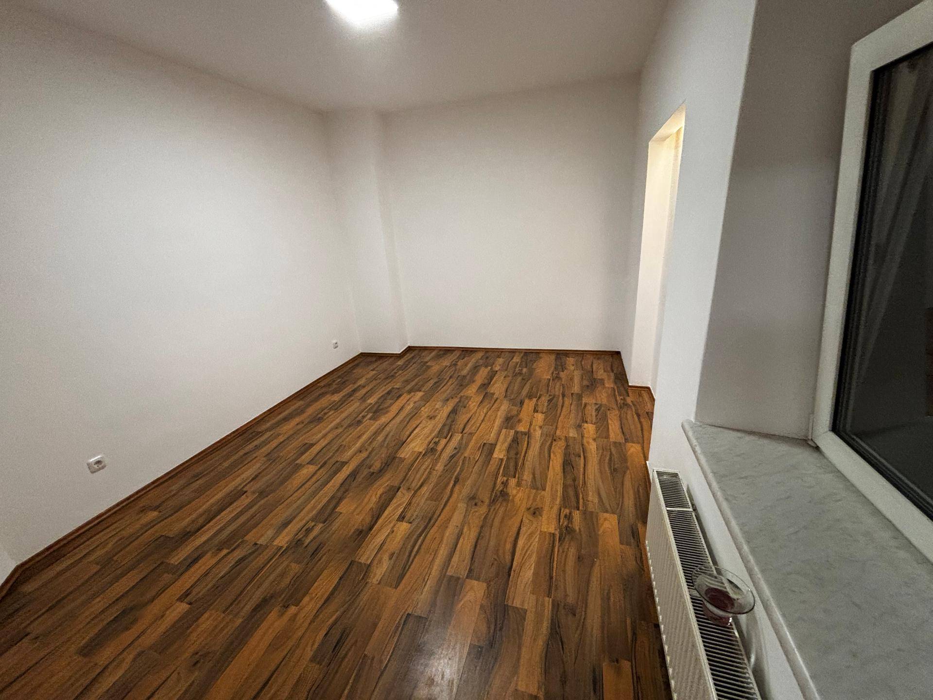 Leeres Zimmer mit Holzboden, weißen Wänden und einem Fenster, bereit zur individuellen Gestaltung.