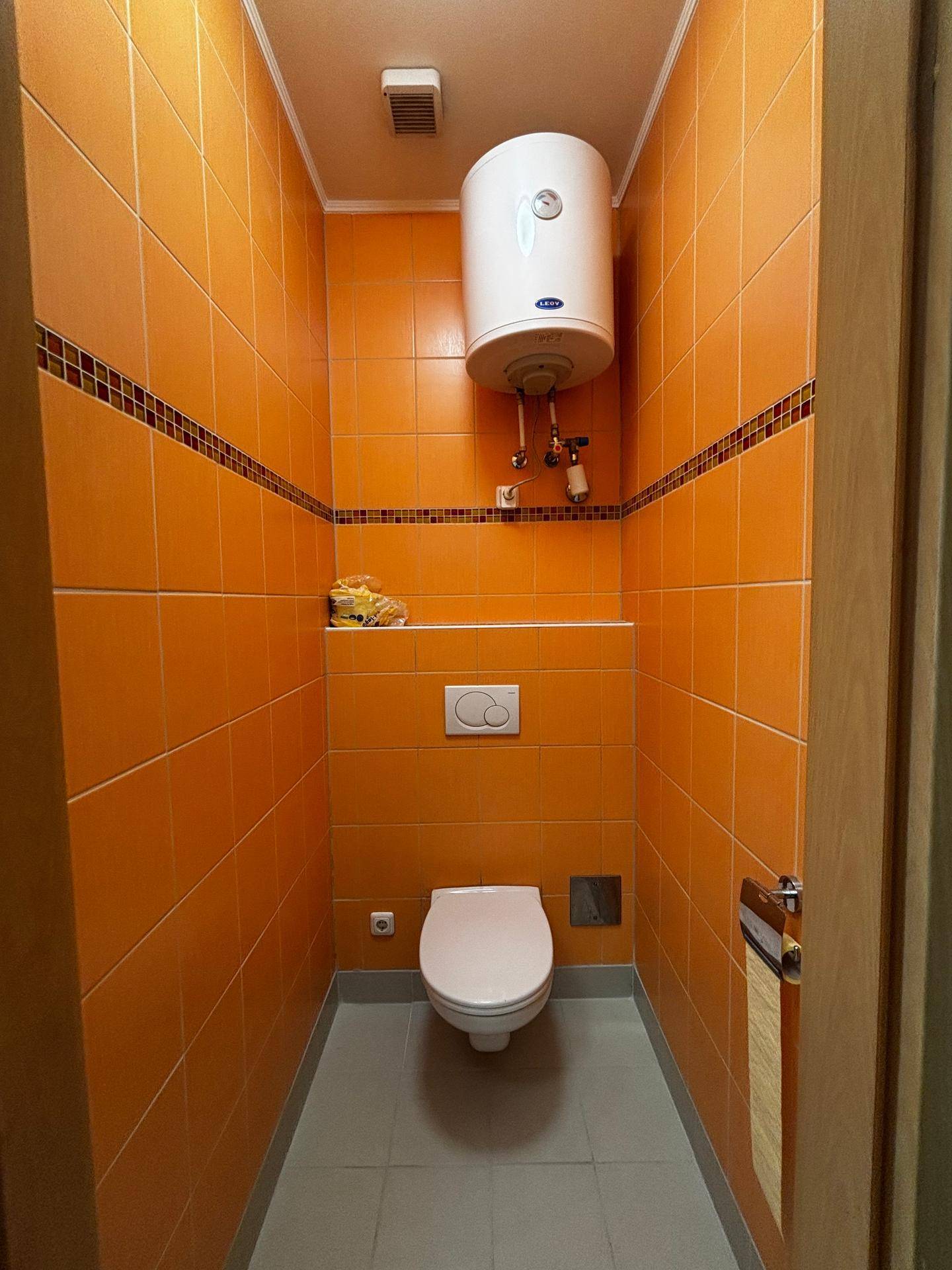 Kleines WC mit leuchtend orangefarbenen Fliesen und wandhängendem WC, funktional und farbenfroh gestaltet.
