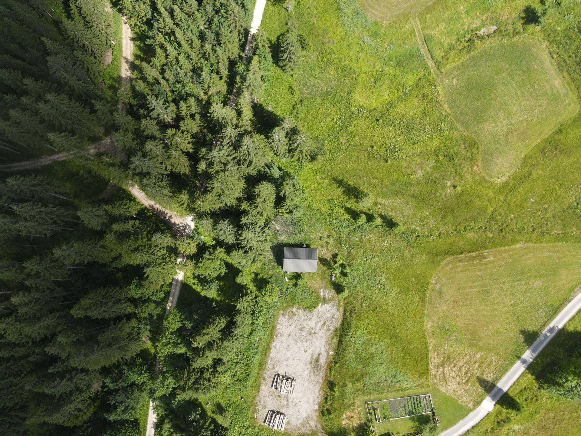 Weitläufige Luftaufnahme des Grundstücks mit Hütte, umgeben von Wald, Wiesen und Zufahrtswegen.