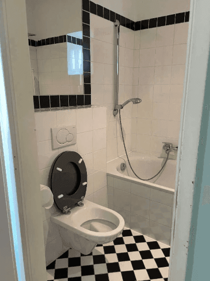 Badezimmer mit Toilette, Badewanne und markantem Schachbrettmuster-Fliesenboden.