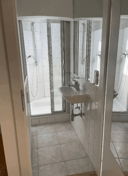 Kleines Badezimmer mit Duschkabine und Waschbecken, funktional und hell gefliest.