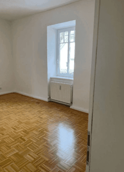 Geräumiges Zimmer mit Parkettboden und Fenster, das viel Tageslicht hereinlässt.