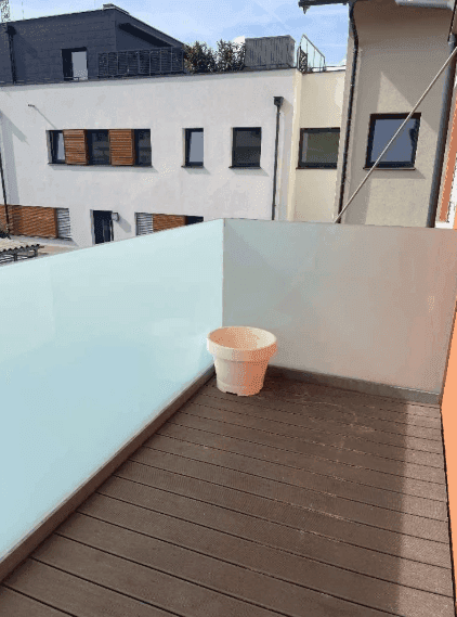 Moderner Balkon mit Holzdielenboden und Blick auf umliegende Gebäude.