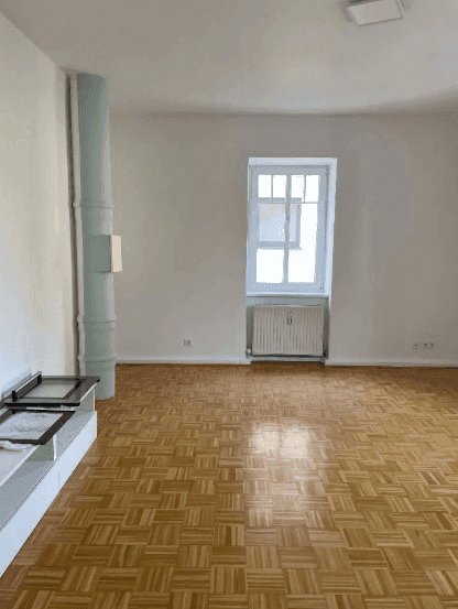 Geräumiges Zimmer mit Parkettboden und Fenster, das viel Tageslicht hereinlässt.