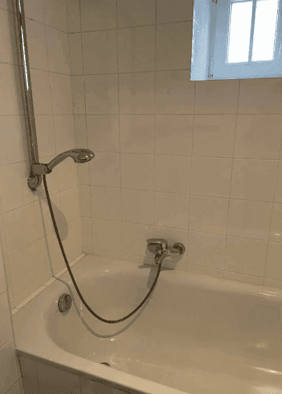 Badezimmer mit Badewanne und Duschvorrichtung, hell gefliest und funktional.