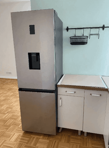 Moderner Kühlschrank neben einer kleinen Küchenzeile in einem hellen Raum.