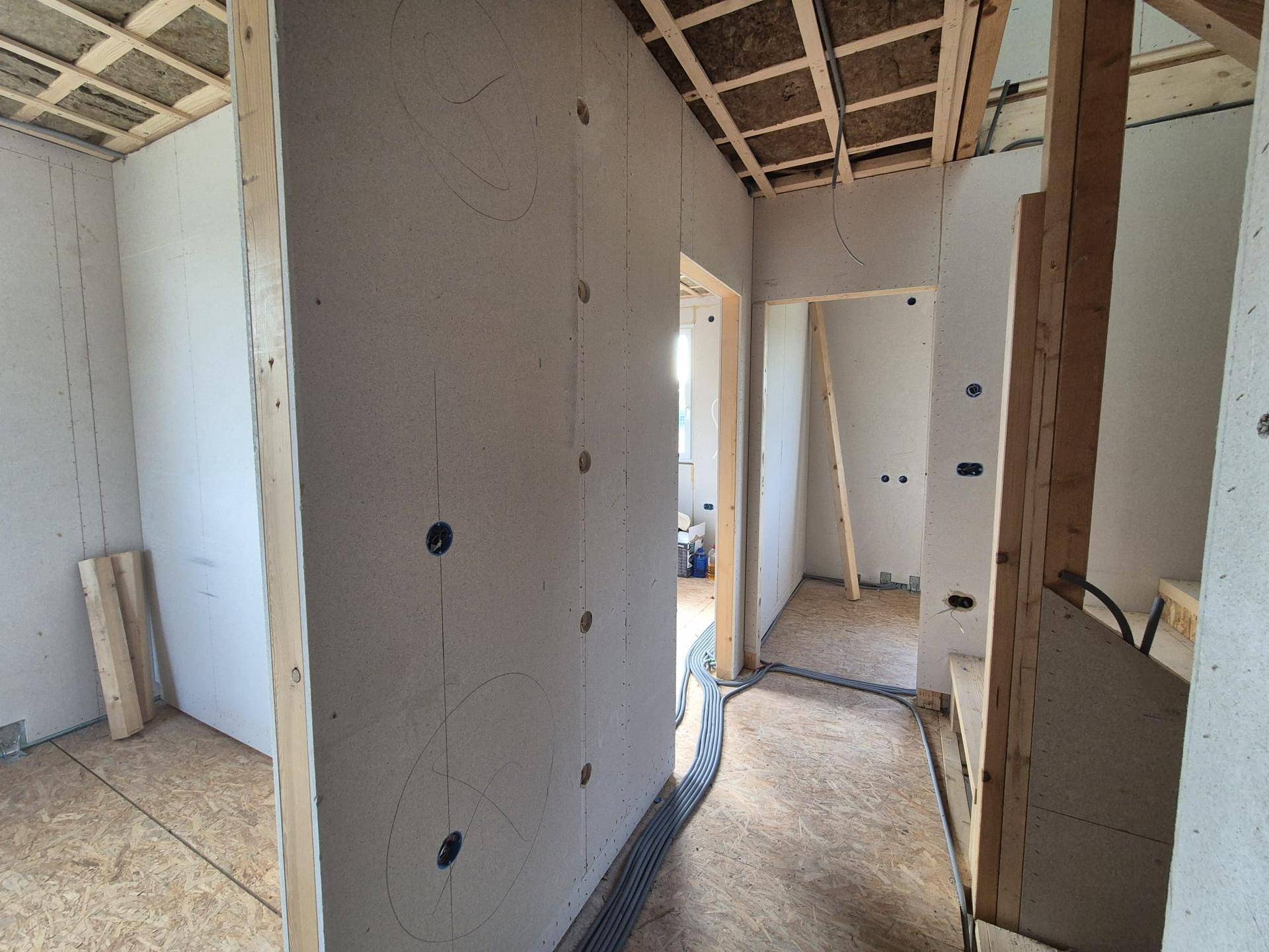 Innenansicht eines Flurbereichs im Rohbau mit Trockenbauwänden und sichtbaren Elektroinstallationen.
