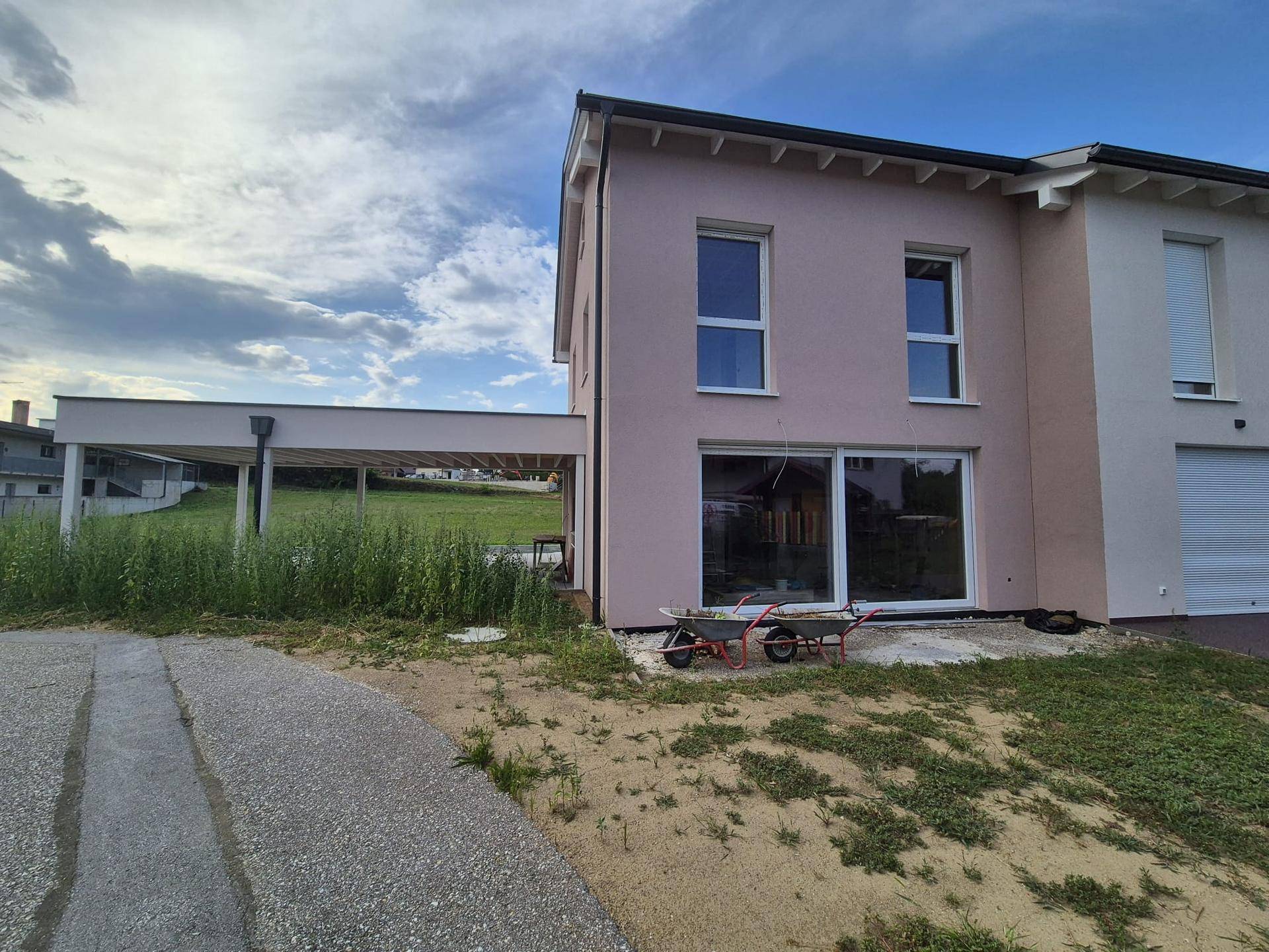 Seitenansicht des Hauses mit großer Glasschiebetür im Erdgeschoss und dem Carport im Hintergrund.