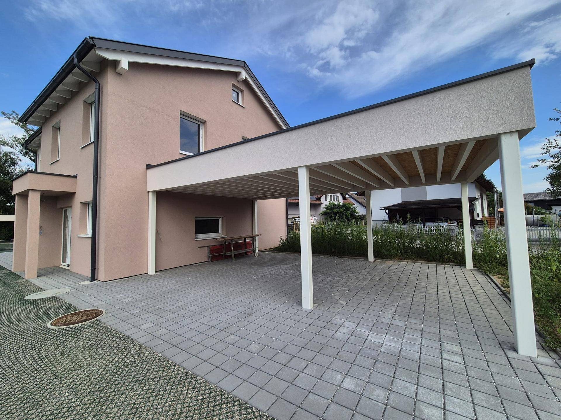Ansicht des modernen Einfamilienhauses mit Carport und gepflasterter Zufahrt unter hellem Himmel.