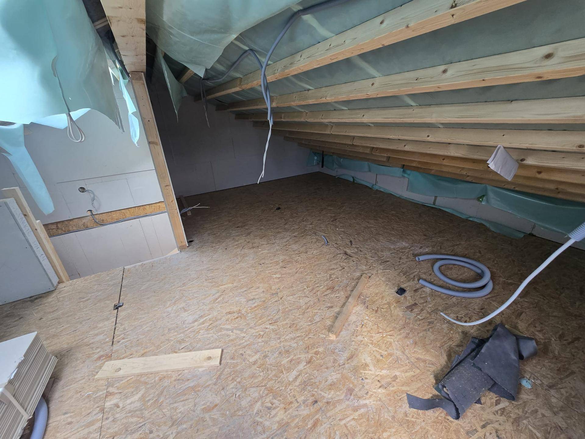 Weiterer Blick in das Dachgeschoss im Rohbau mit Holzbalkenkonstruktion und Isolationsmaterial.