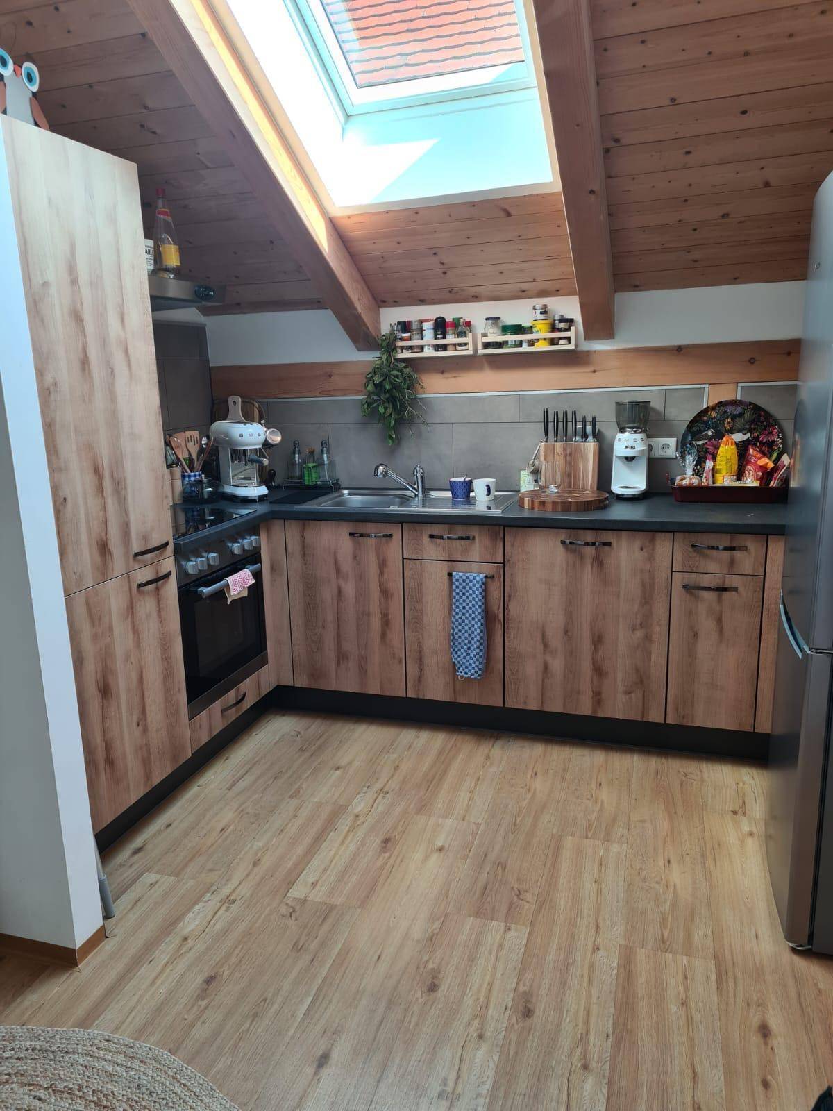 Moderne Küche im Dachgeschoss mit Holzfronten, dunkler Arbeitsplatte und viel Tageslicht durch das Dachfenster.