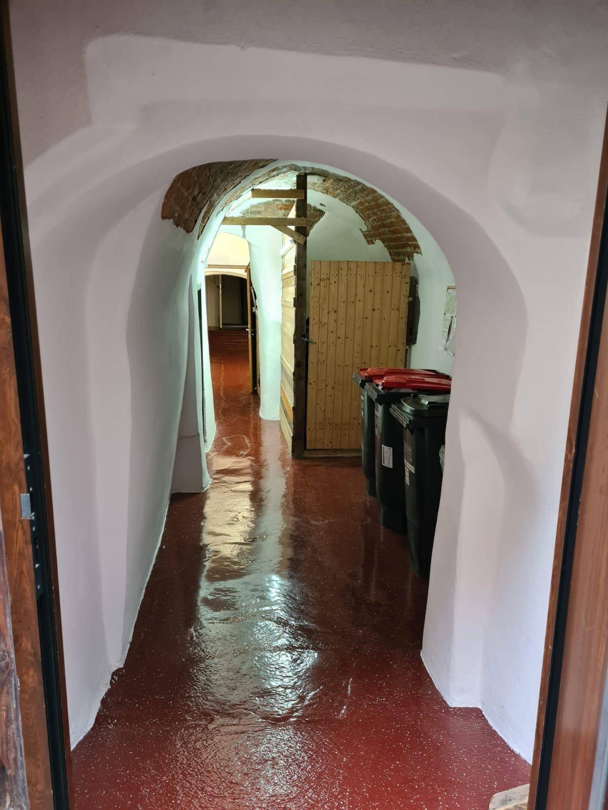 Gewölbter Kellerflur mit glänzendem roten Boden und sichtbaren Ziegeln im Bogenbereich.