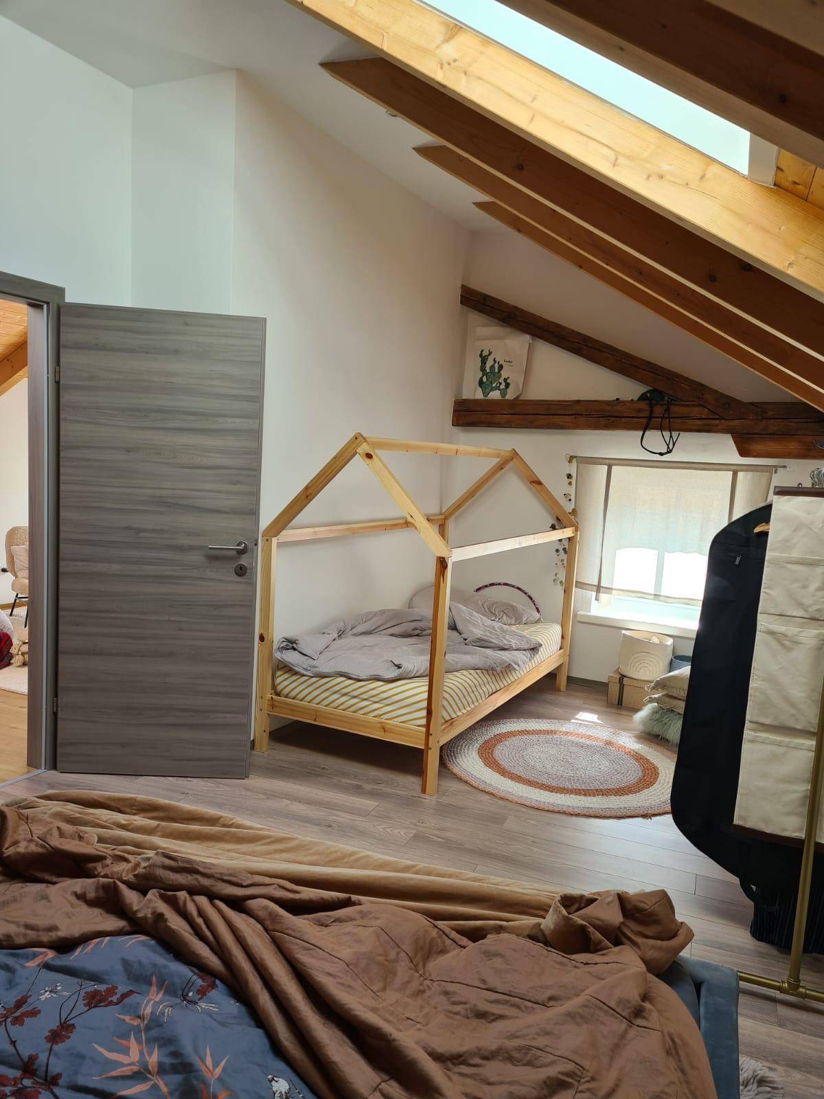 Helles Kinderzimmer im Dachgeschoss mit einzigartigem Hausbett, Holzbalken und viel Tageslicht durch das Dachfenster.