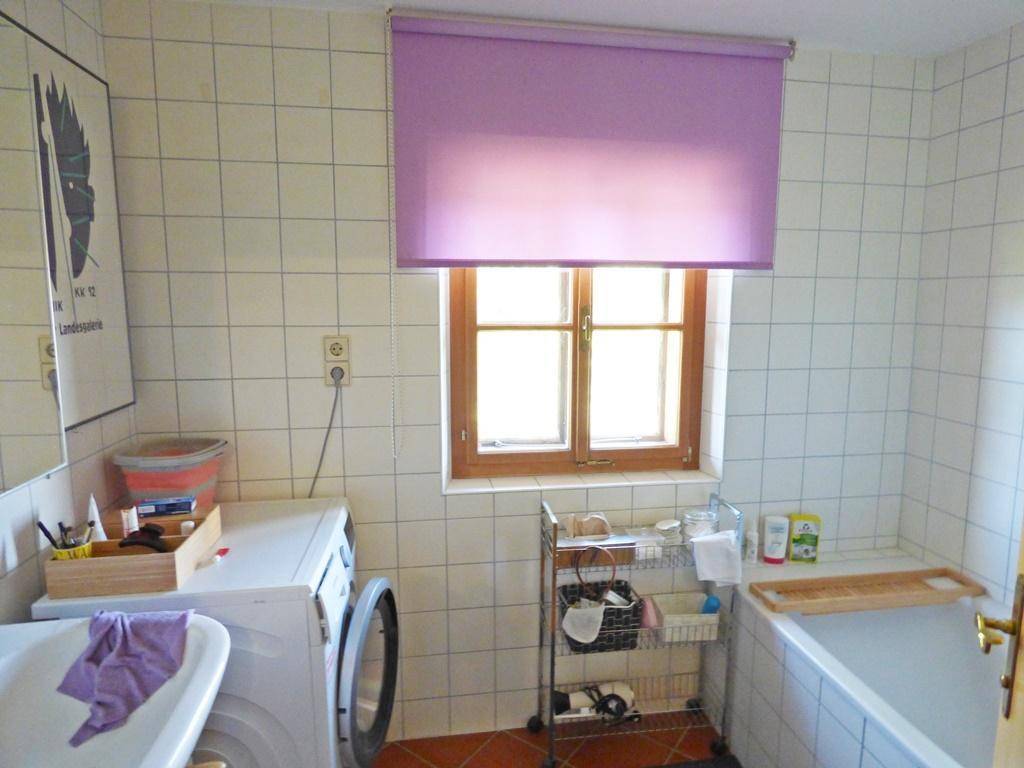 Badezimmer mit Waschmaschine, Badewanne und gefliesten Wänden.