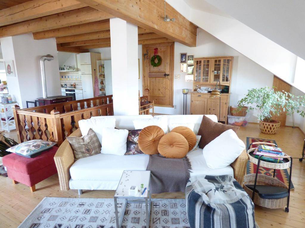 Gemütliches Wohnzimmer im Dachgeschoss mit Holzbalken, Sofa und Blick zur Küche.